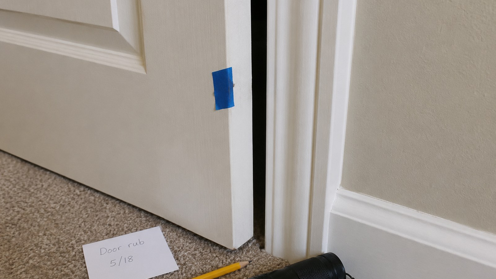 Interior apartment door edge with hinge screws, painter tape marking a rub spot, and simple hand tools.
