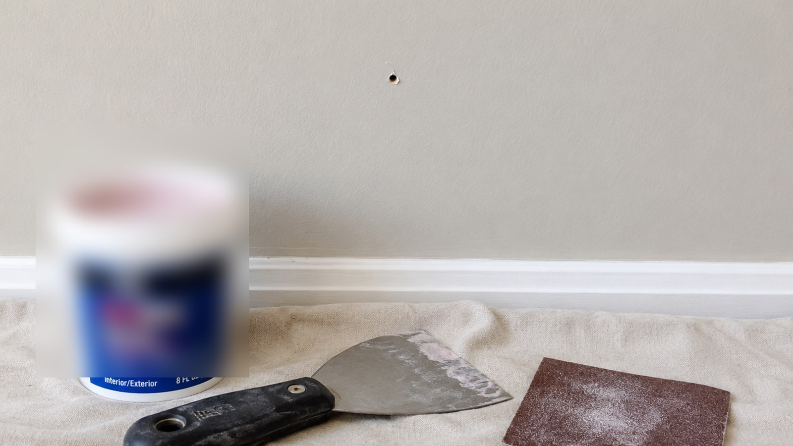 Small drywall holes with patching putty, a putty knife, painter tape, and a drop cloth.