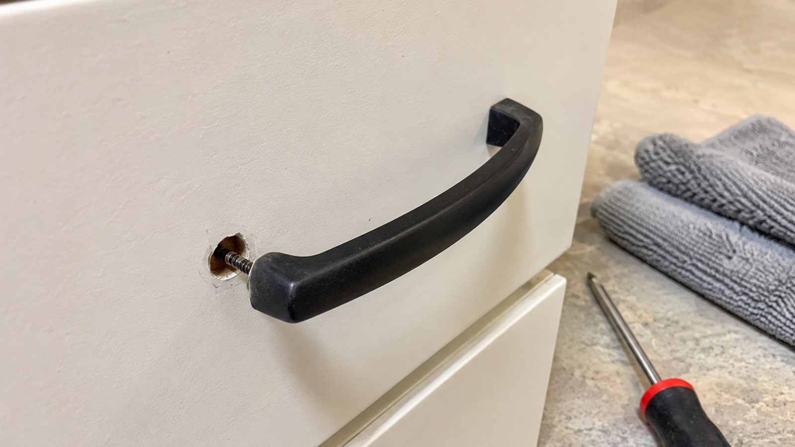 Cabinet drawer pull with a screwdriver, soft cloth, and small bowl for screws.