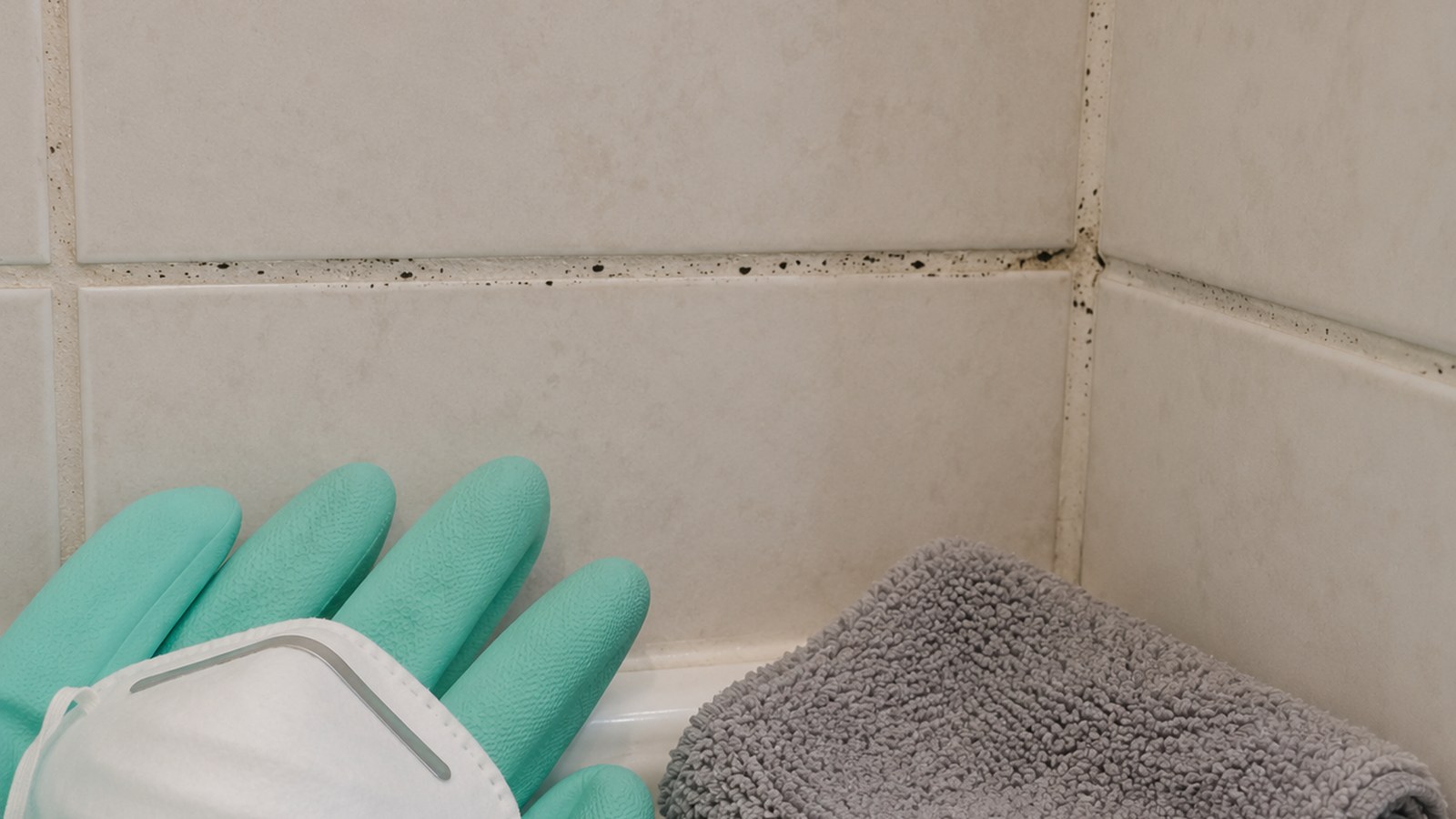 Small bathroom tile area with a few dark surface spots, gloves, mask, brush, and phone for documentation.