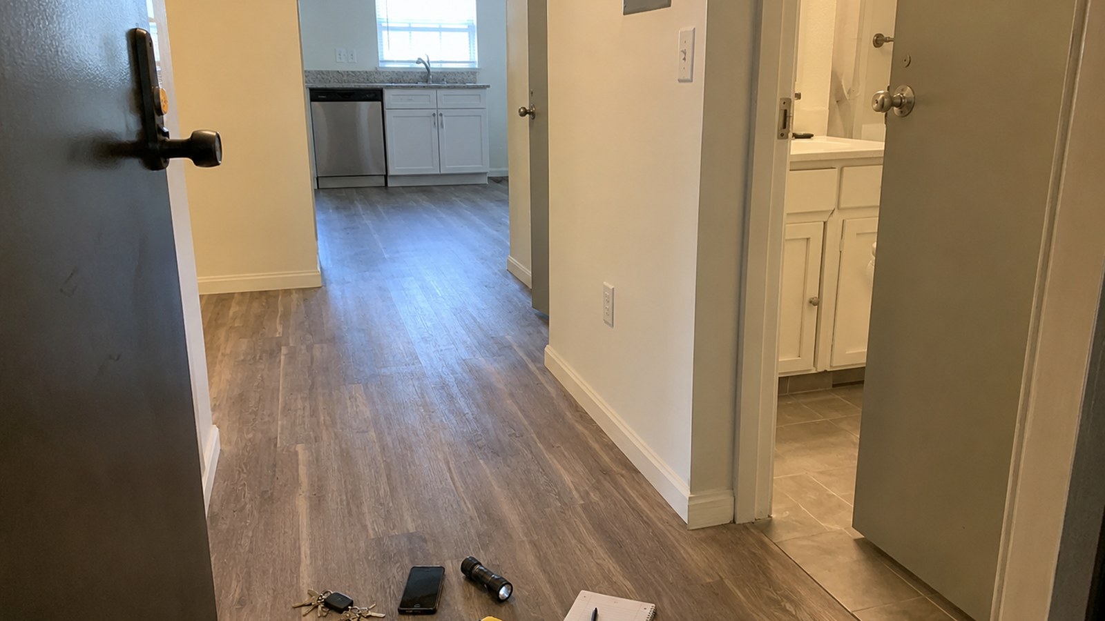 First apartment maintenance walkthrough setup with keys, phone, flashlight, painter tape, notebook, and open sink cabinet.