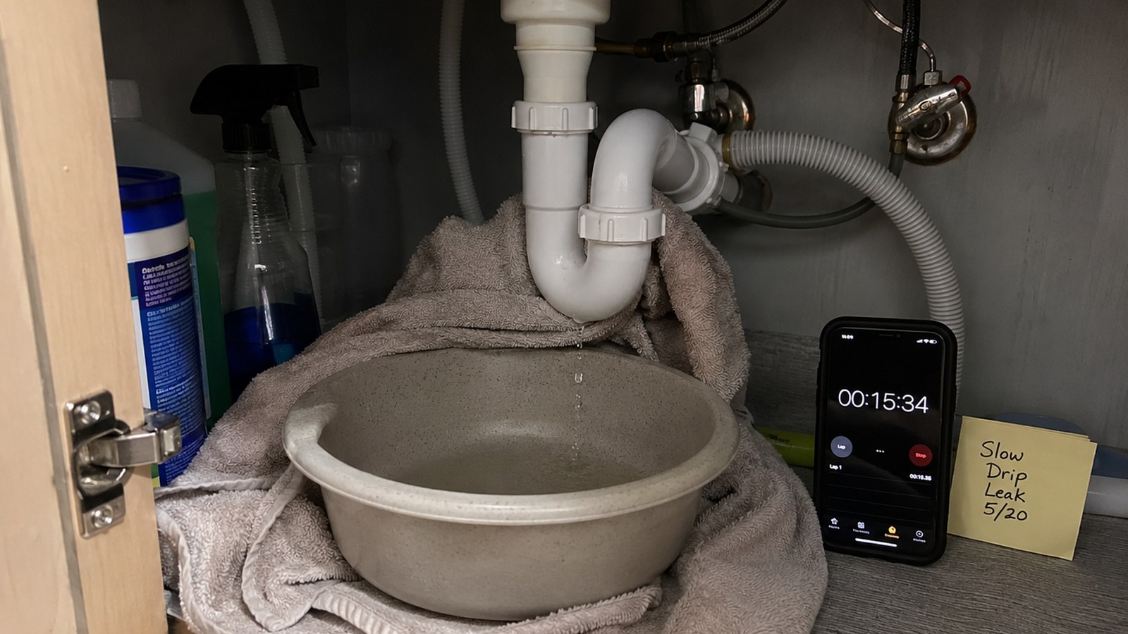 Small water leak containment setup showing a bowl, towels, painter tape marking water spread, flashlight, and phone.